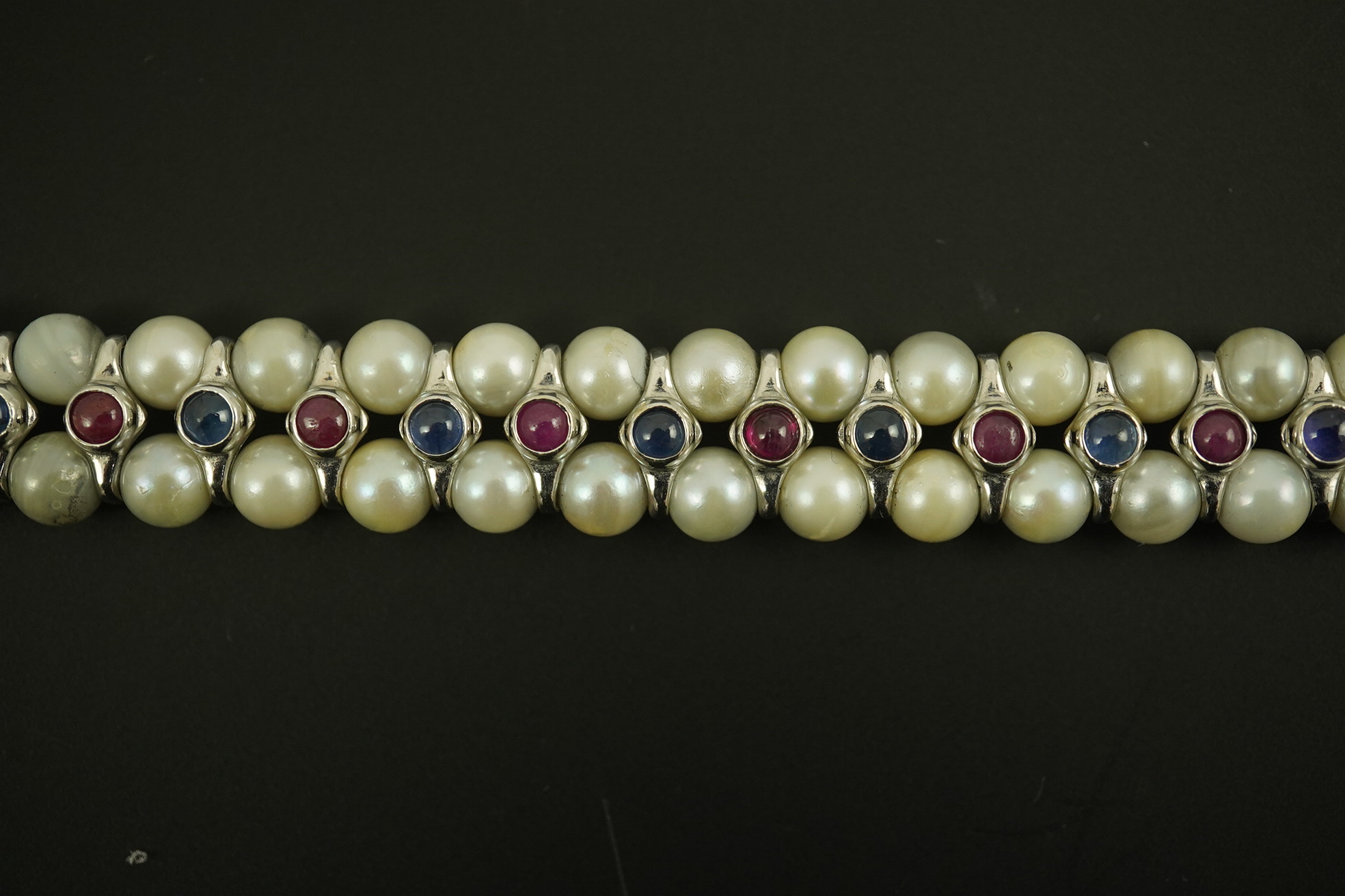 A late 20th century 18k white gold and two row cultured pearl bracelet, set with single row of cabochon rubies and sapphires